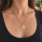 Goldfarbene Relic Coin Halskette an einer Frau mit dunklem Oberteil; digitales Initialenkreuz. all-groups