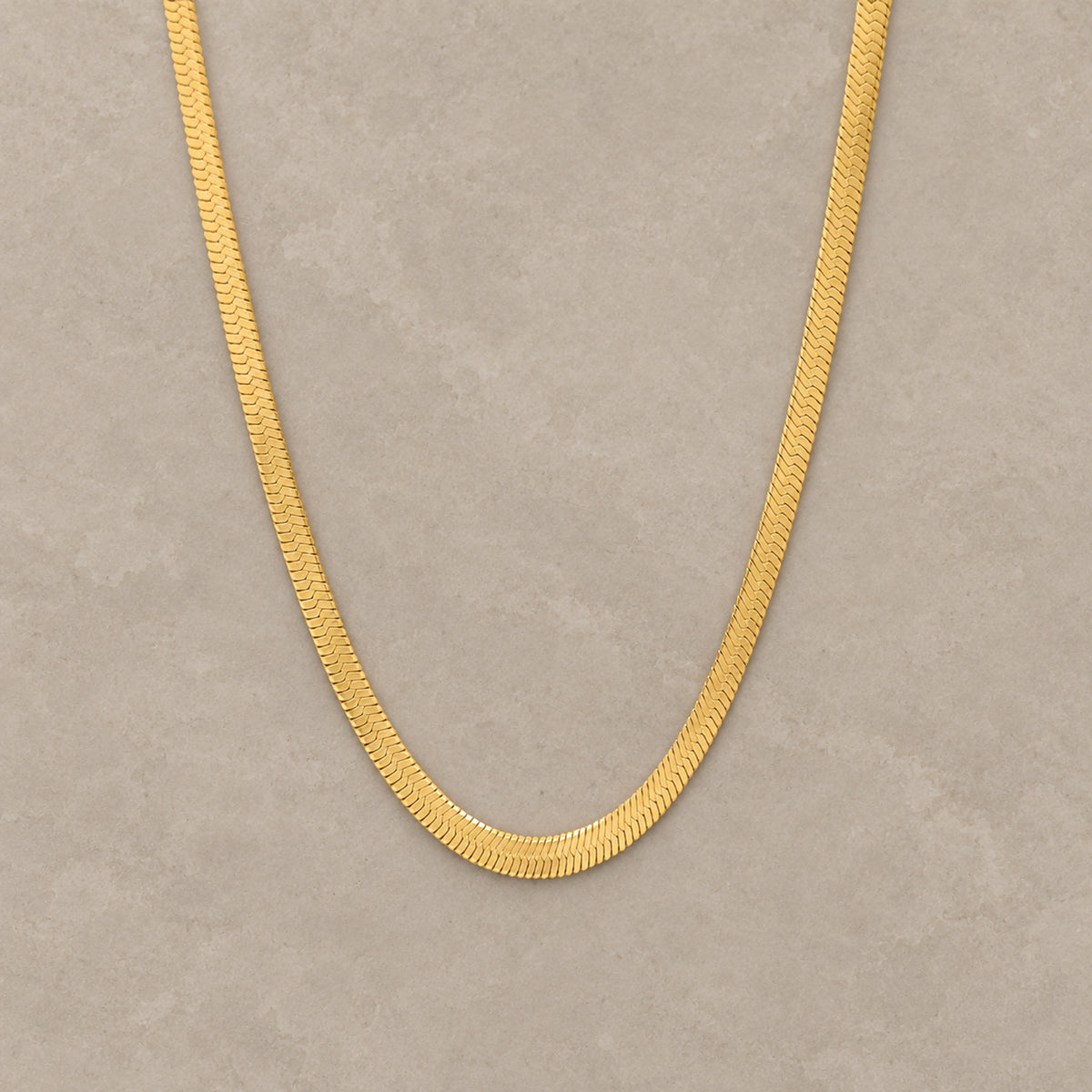 Sleek Chain in Gold auf warmem mineralischem Untergrund
